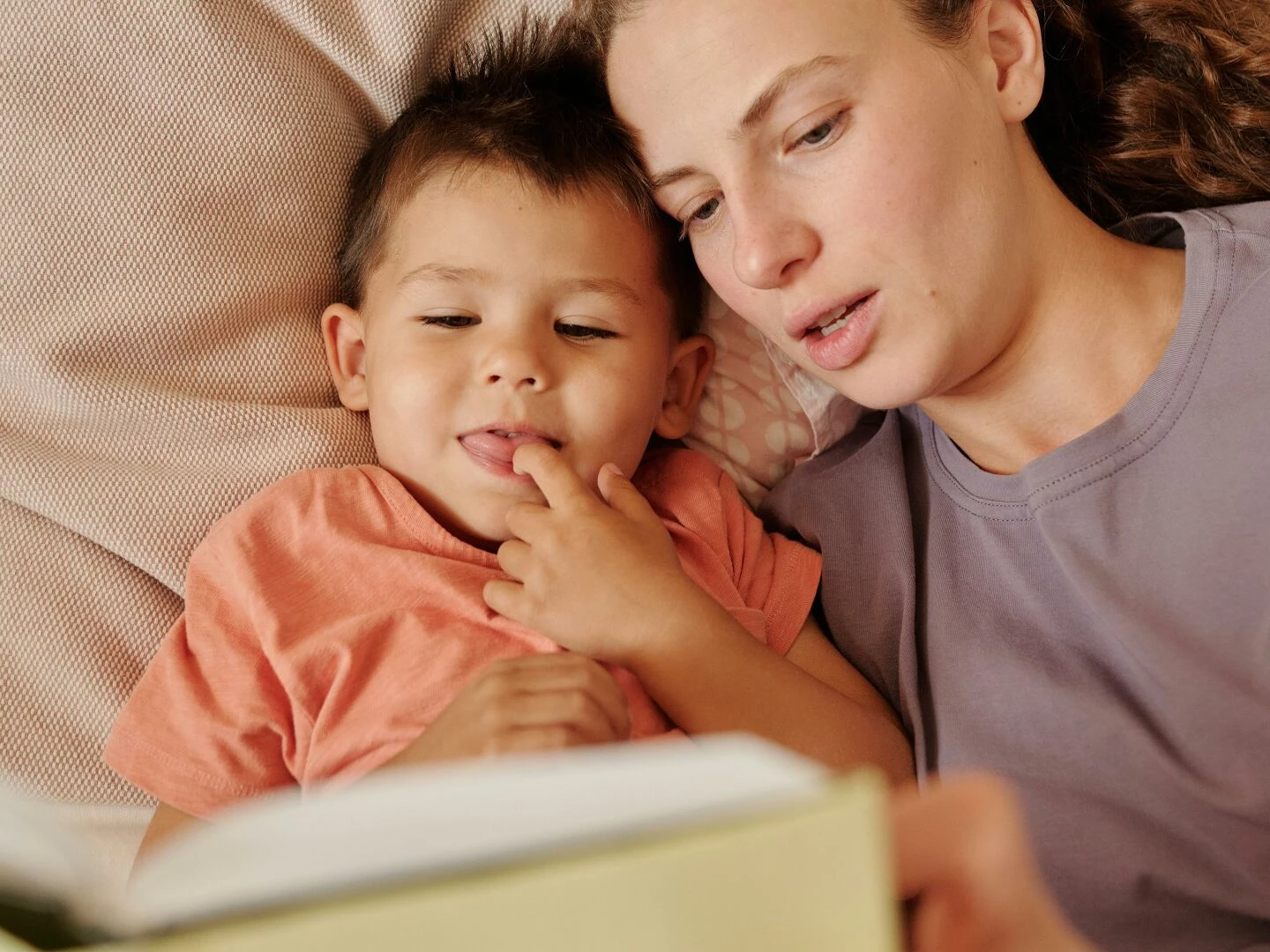 a loving mother and her young son enjoy reading a book together in bed captured in a cozy home setting