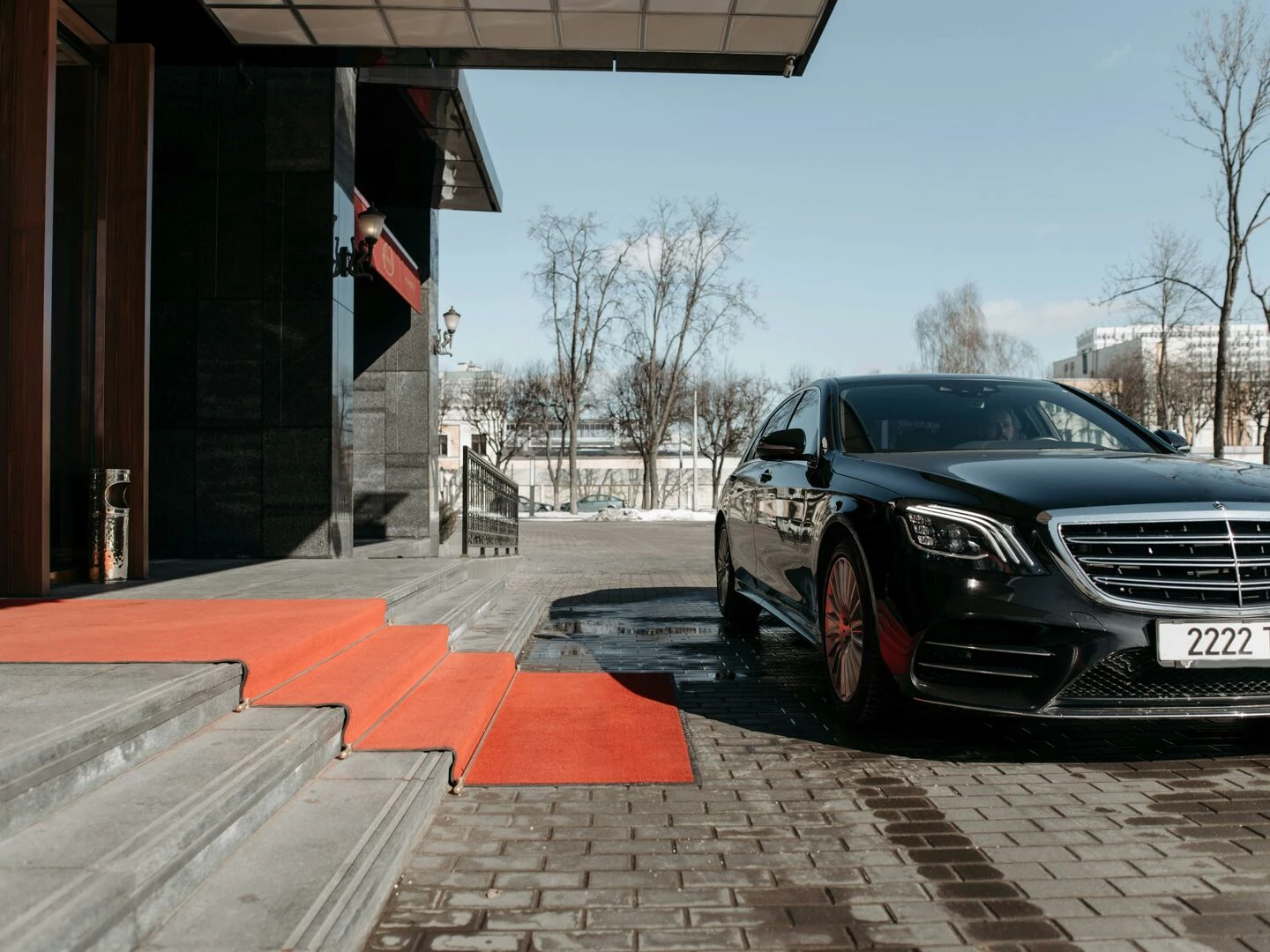 a luxury black sedan parked on a red carpet driveway outside a modern building