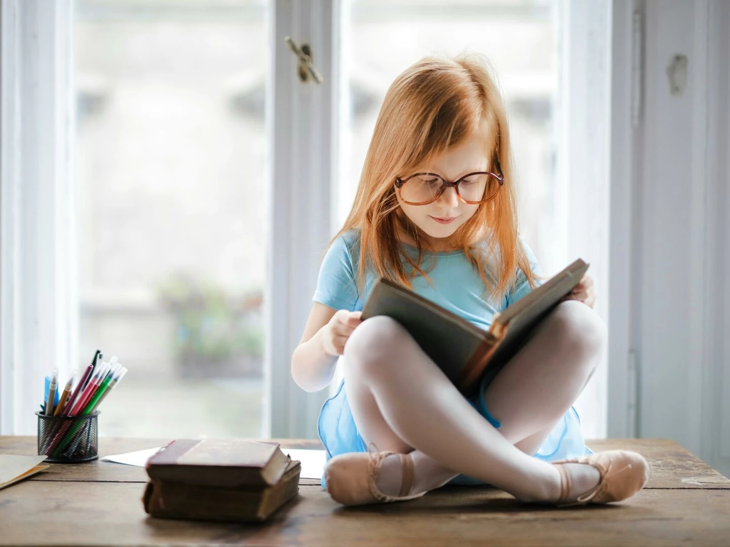 adorable young girl wearing glasses reading a book indoors by a window captures innocence and focus