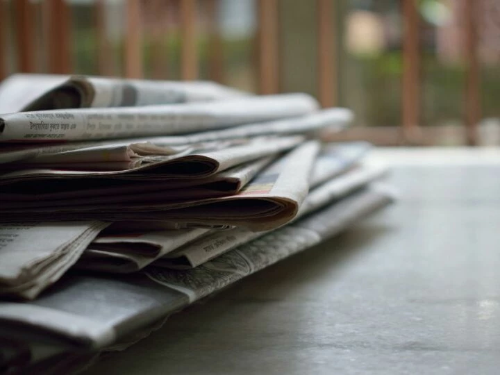 A close-up of a stack of newspapers resting on a desk, symbolizing information and media.