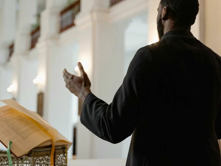 A priest delivers a sermon inside a beautifully lit church, standing at an altar.