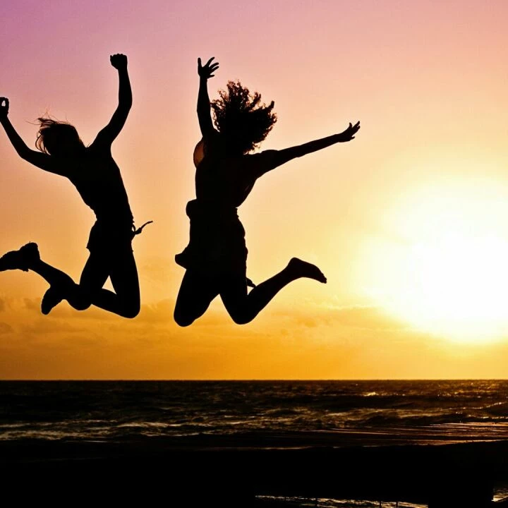 Silhouettes of two people joyfully jumping on a beach during a vibrant sunset.