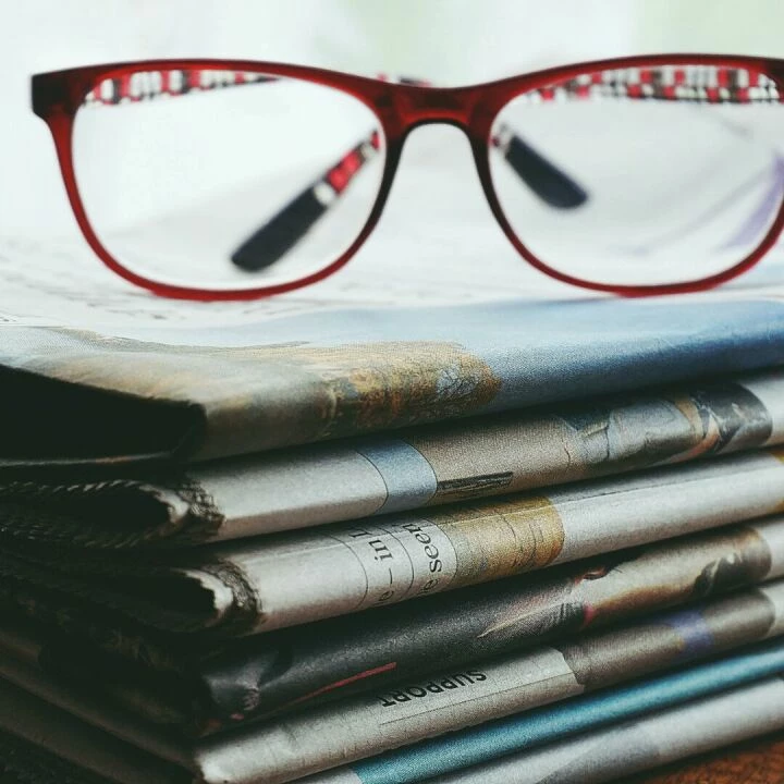 Red eyeglasses resting on a stack of newspapers symbolize reading and information.