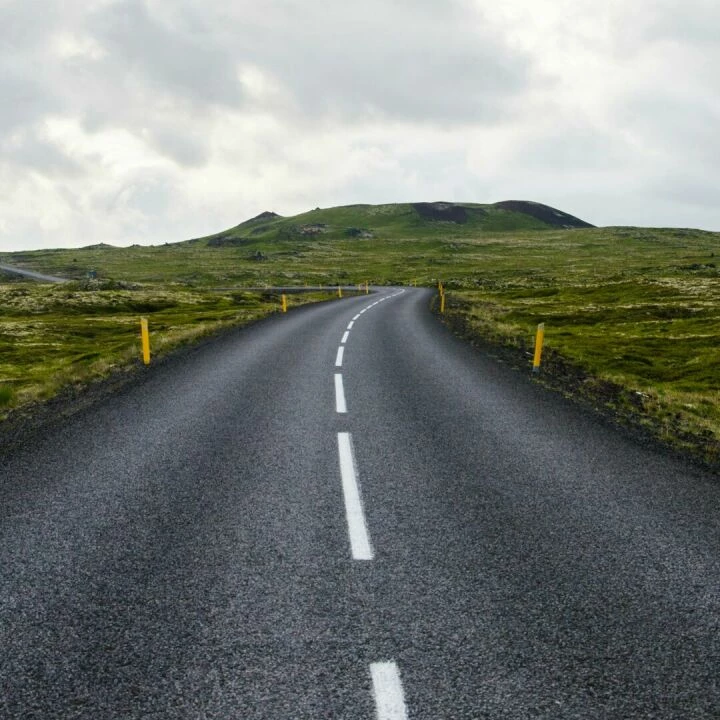 Empty road stretches through lush countryside under cloudy skies, ideal for travel themes.