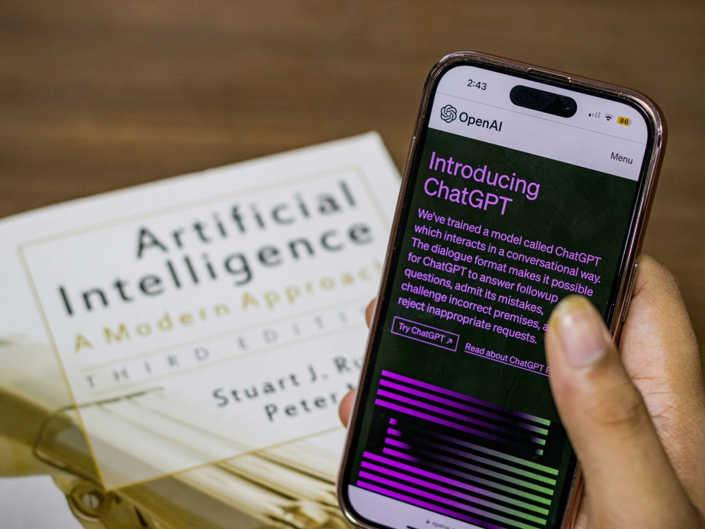 closeup of a smartphone displaying chatgpt app held over ai textbook