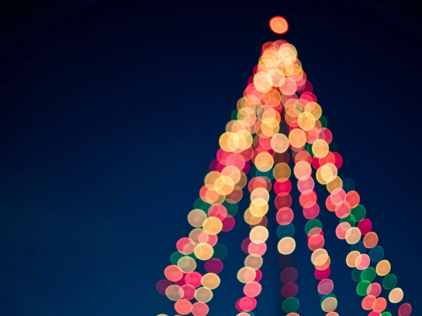 colorful bokeh lights forming a christmas tree against a dark blue sky