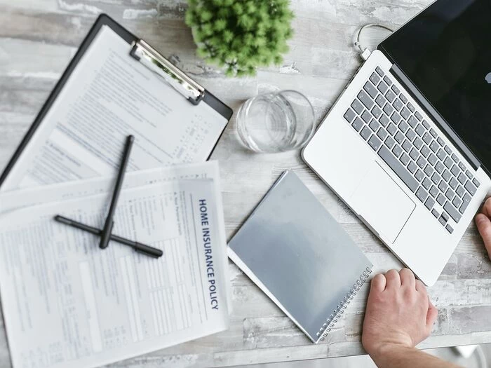 person writing on white paper beside clear glass mug and silver macbook