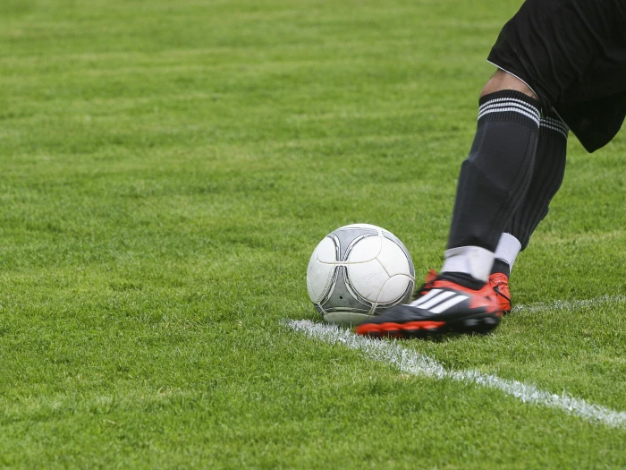 soccer player kicking white gray soccer ball on green grass field